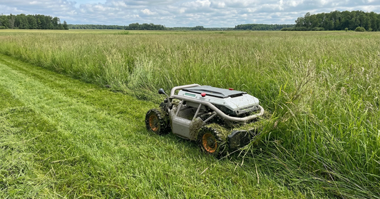 Ein fortschrittlicher Mähroboter bahnt sich effizient einen Weg durch eine riesige, wilde Wiese mit extrem hohem Gras unter bewölktem Himmel und zeigt professionelles Vegetationsmanagement im Außenbereich.