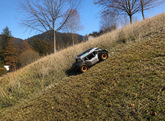 Ein Mowrator-Mähroboter mäht einen Herbst-Rasen vor dem Winter, während im Hintergrund ein Bauernhaus und sanft geschwungene Hügel zu sehen sind.
